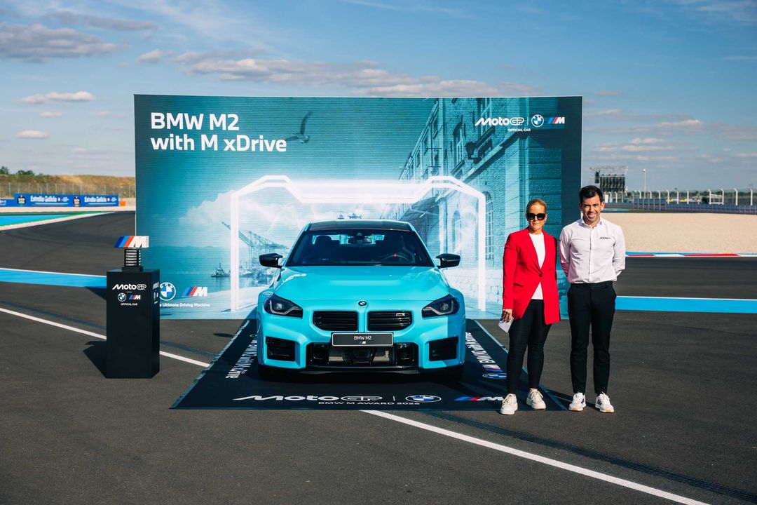 BMW M2 z napędem M xDrive — przód, prezentacja pojazdu na torze wyścigowym w otoczeniu osób i banera promocyjnego