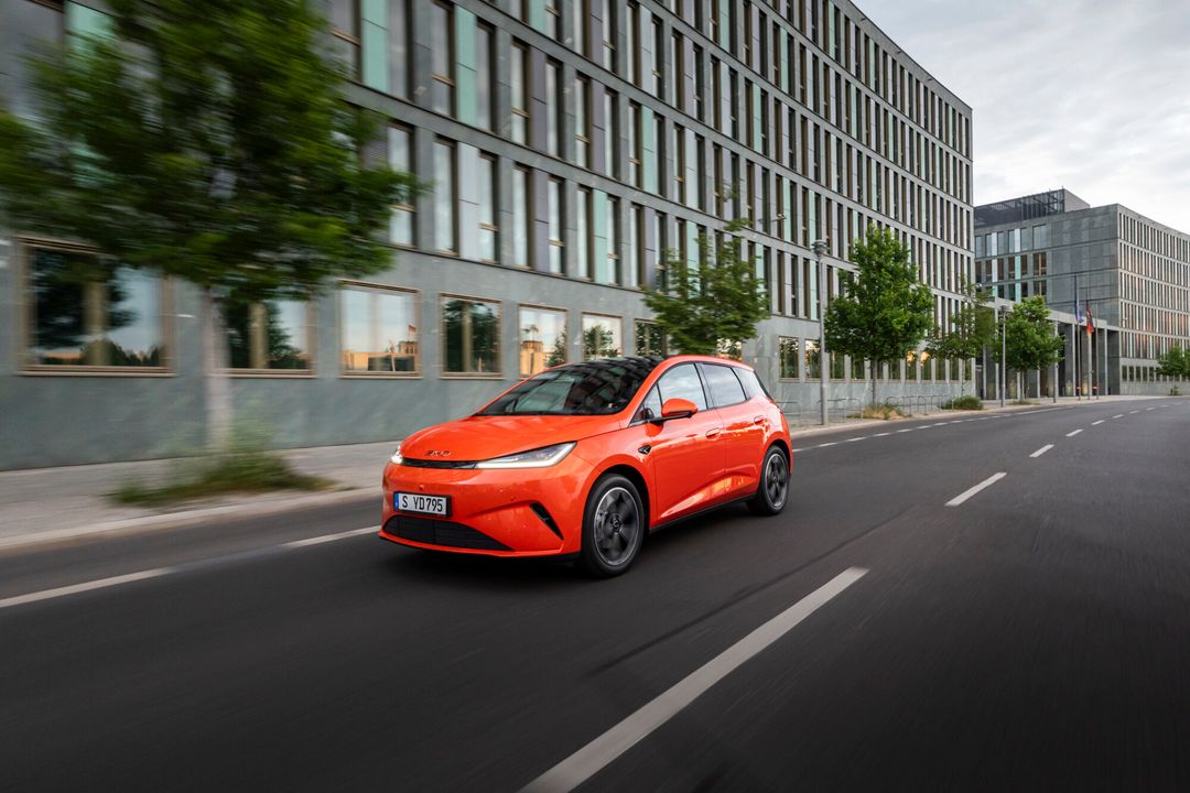 BYD Dolphin G DM-i — przód 3/4, dynamiczna jazda miejska, kolor pomarańczowy, niemiecka tablica rejestracyjna