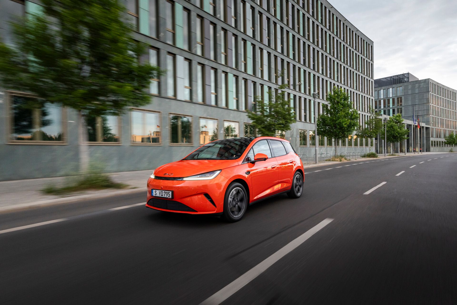 BYD Dolphin G DM-i — przód 3/4, dynamiczna jazda miejska, kolor pomarańczowy, niemiecka tablica rejestracyjna