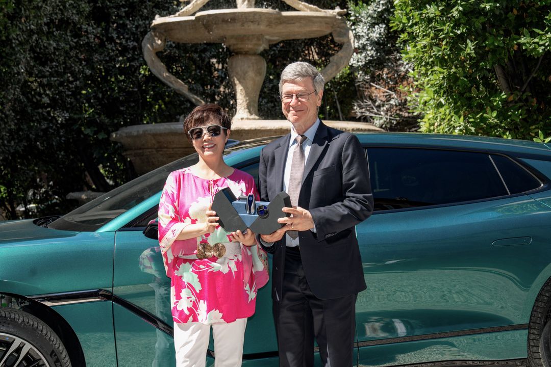 DENZA Z9GT — ceremonia przekazania kluczy w rzymskim ogrodzie, dwie osoby z trofeami, auto widoczne w tle