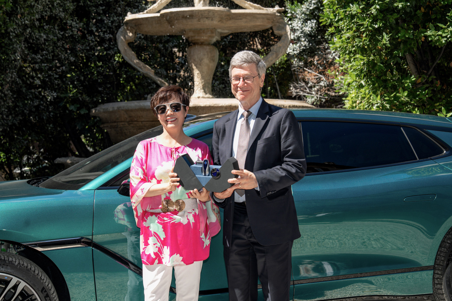 DENZA Z9GT — ceremonia przekazania kluczy w rzymskim ogrodzie, dwie osoby z trofeami, auto widoczne w tle