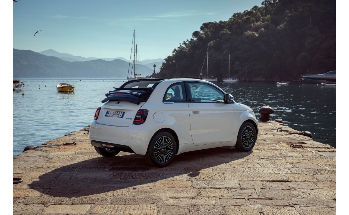 Fiat 500 Dolcevita Cabrio — widok od tyłu 3/4, dach całkowicie otwarty, zaparkowany na kamiennym molo nad zatoką z żaglówkami w tle