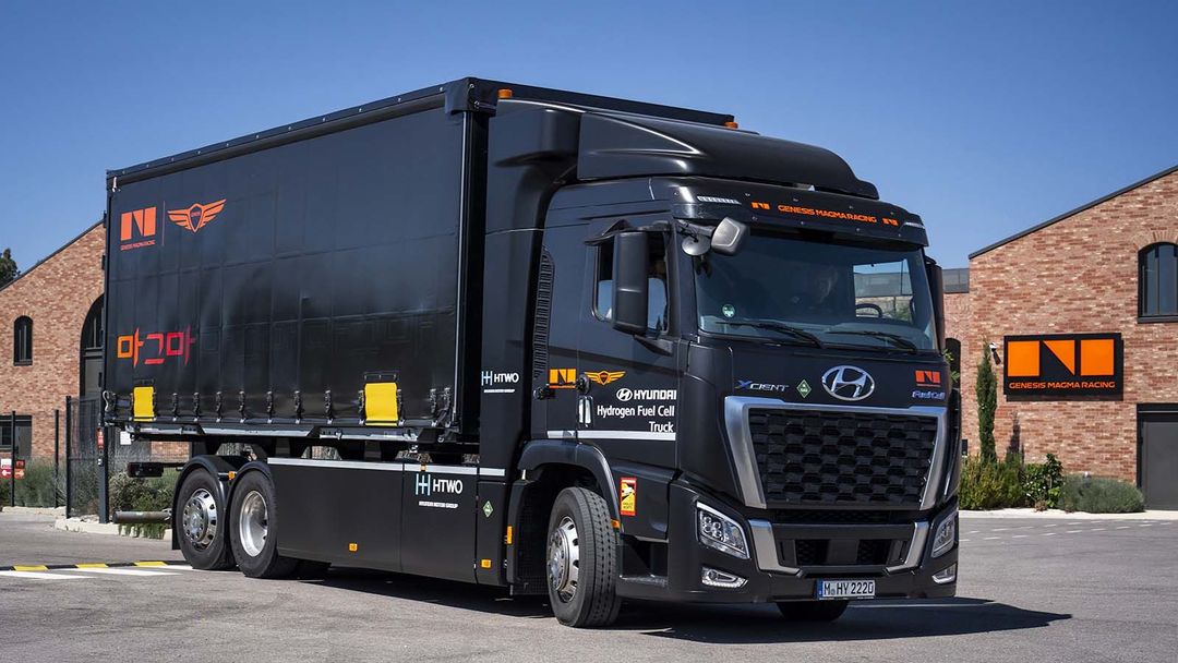 Hyundai Xcient Fuel Cell w barwach Genesis Magma Racing — bok, na tle hali serwisowej