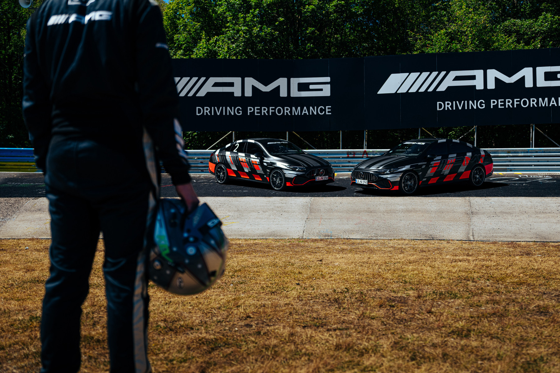 Kierowca testowy z kaskiem przed startem, w tle dwa prototypy Mercedes-AMG CLA 45 na torze