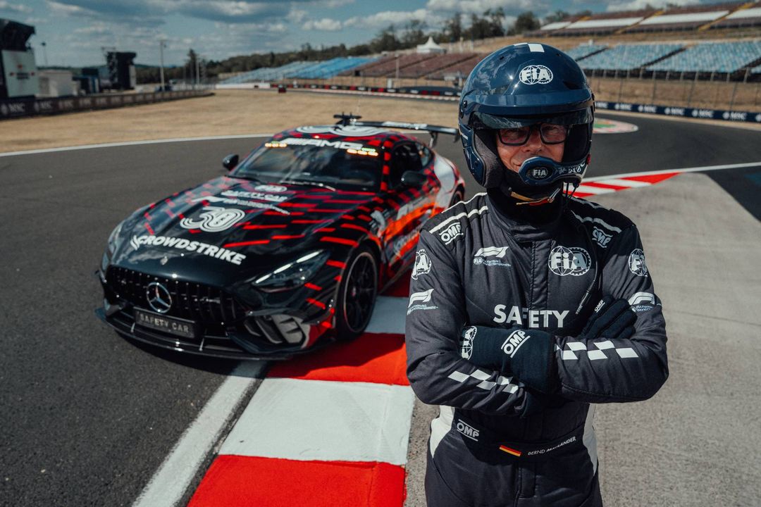 Kierowca safety car w kombinezonie FIA na tle zaparkowanego Mercedesa-AMG GT 63 PRO z podniesionym skrzydłem