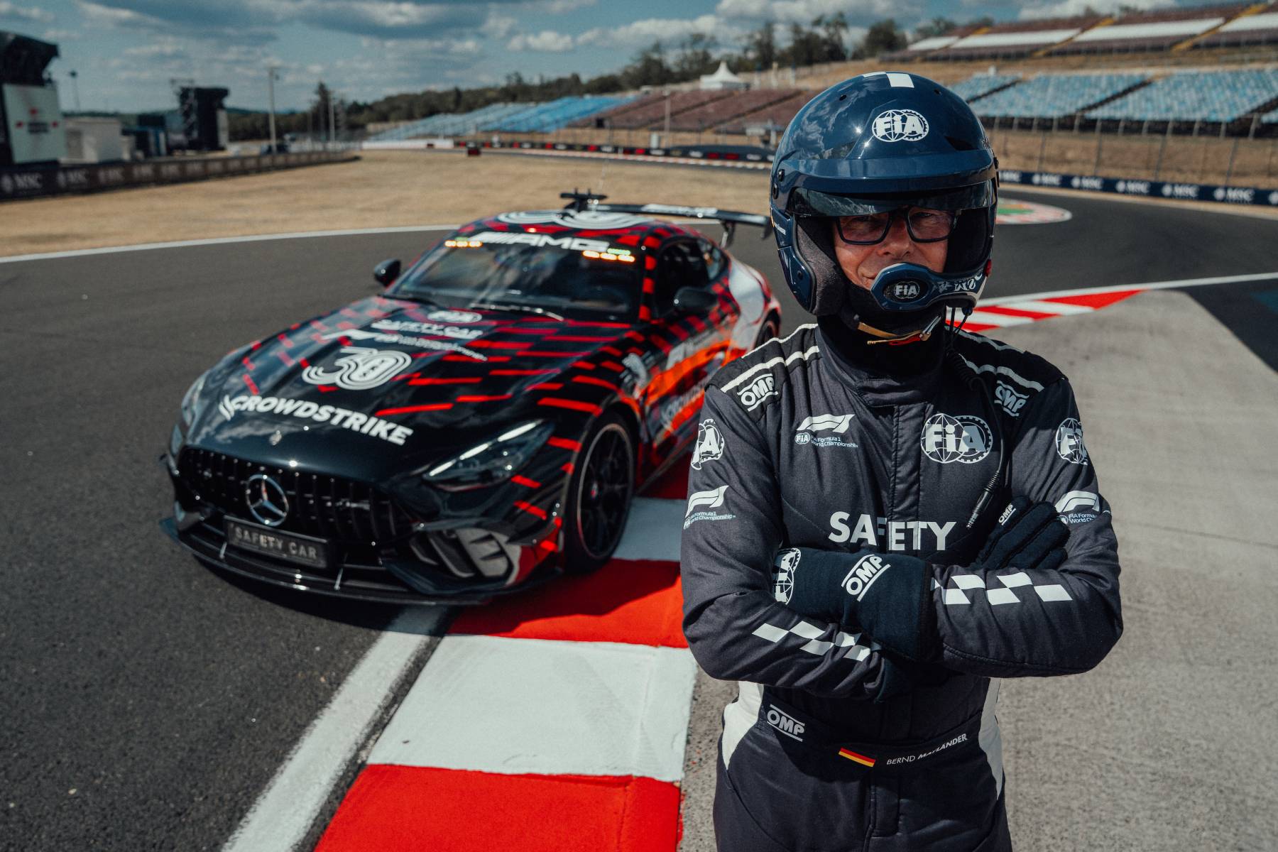 Kierowca safety car w kombinezonie FIA na tle zaparkowanego Mercedesa-AMG GT 63 PRO z podniesionym skrzydłem