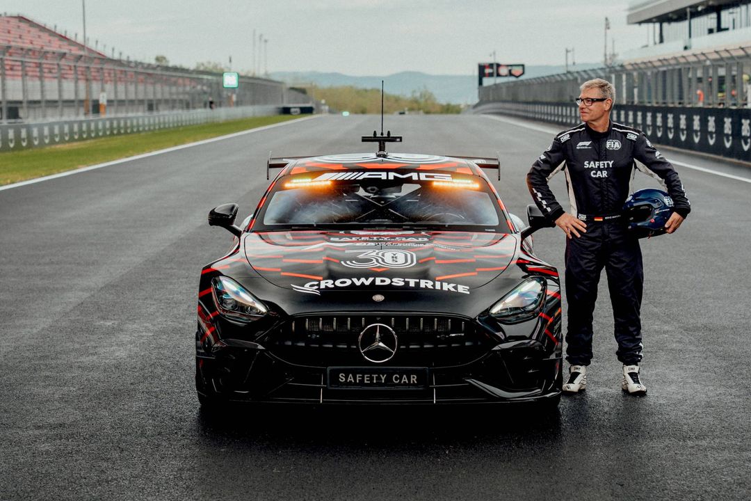 Kierowca safety car z kaskiem w dłoni stojący przy Mercedesie-AMG GT 63 PRO z włączonymi światłami o zmierzchu
