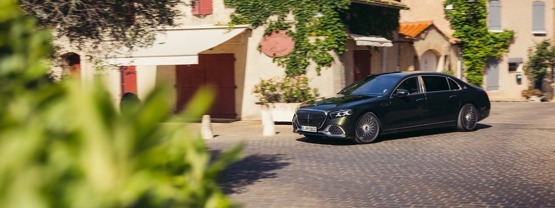 Mercedes-Maybach Klasa S — przód i lewy bok, przejazd przez brukowany plac przy zabytkowej kamienicy (kadr przycięty, panoramiczny)