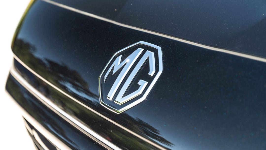 MG — zbliżenie na logo marki i grill na masce ciemnego samochodu