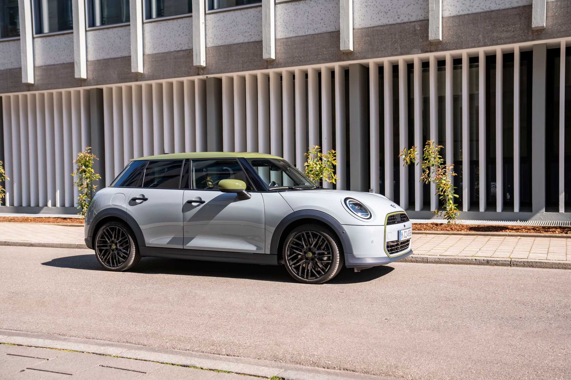 MINI Cooper Paul Smith Edition — bok, srebrne nadwozie z oliwkowym dachem, ujęcie miejskie przy elewacji budynku