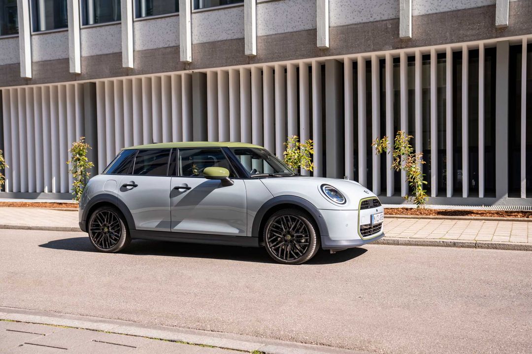 MINI Cooper Paul Smith Edition — bok, srebrny nadwozie z zielonym dachem na tle nowoczesnej fasady budynku