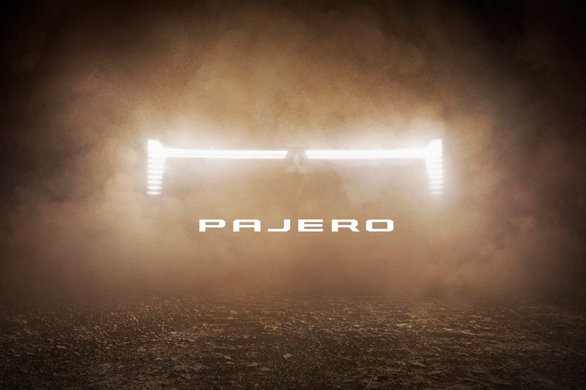 Mitsubishi Pajero 2026 — teaser: świetlne logo lamp przednich na ciemnym, zakurzonym tle, cieplejsza tonacja