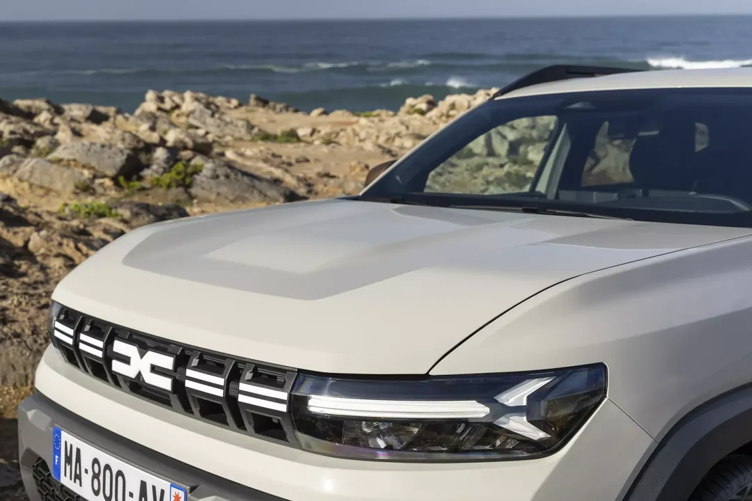 Dacia Duster — zbliżenie na maskę, grill i reflektor LED, w tle skalisty brzeg morza