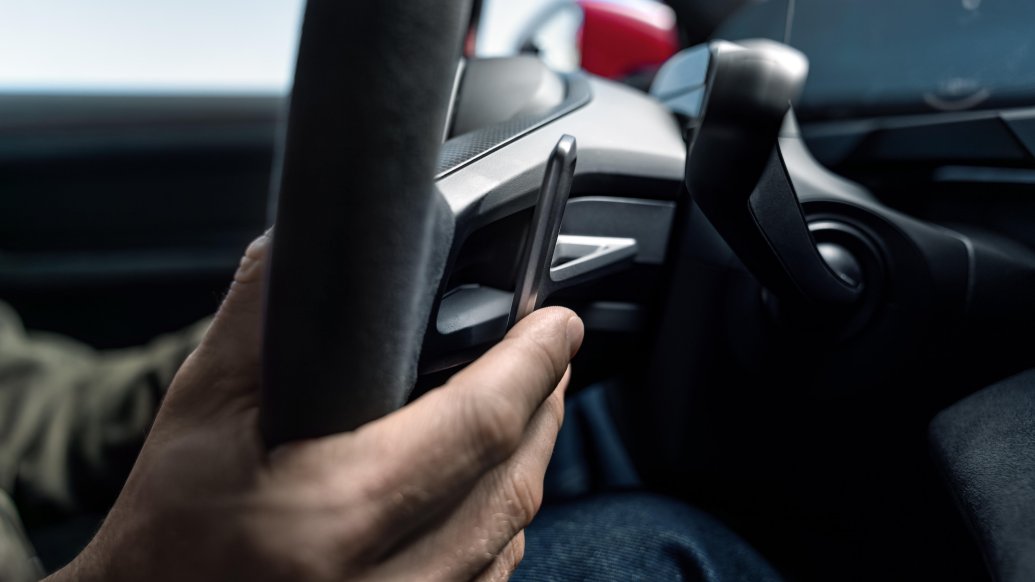Porsche Taycan — dłoń kierowcy przy łopatce E-Shift przy kierownicy, w tle czerwone nadwozie