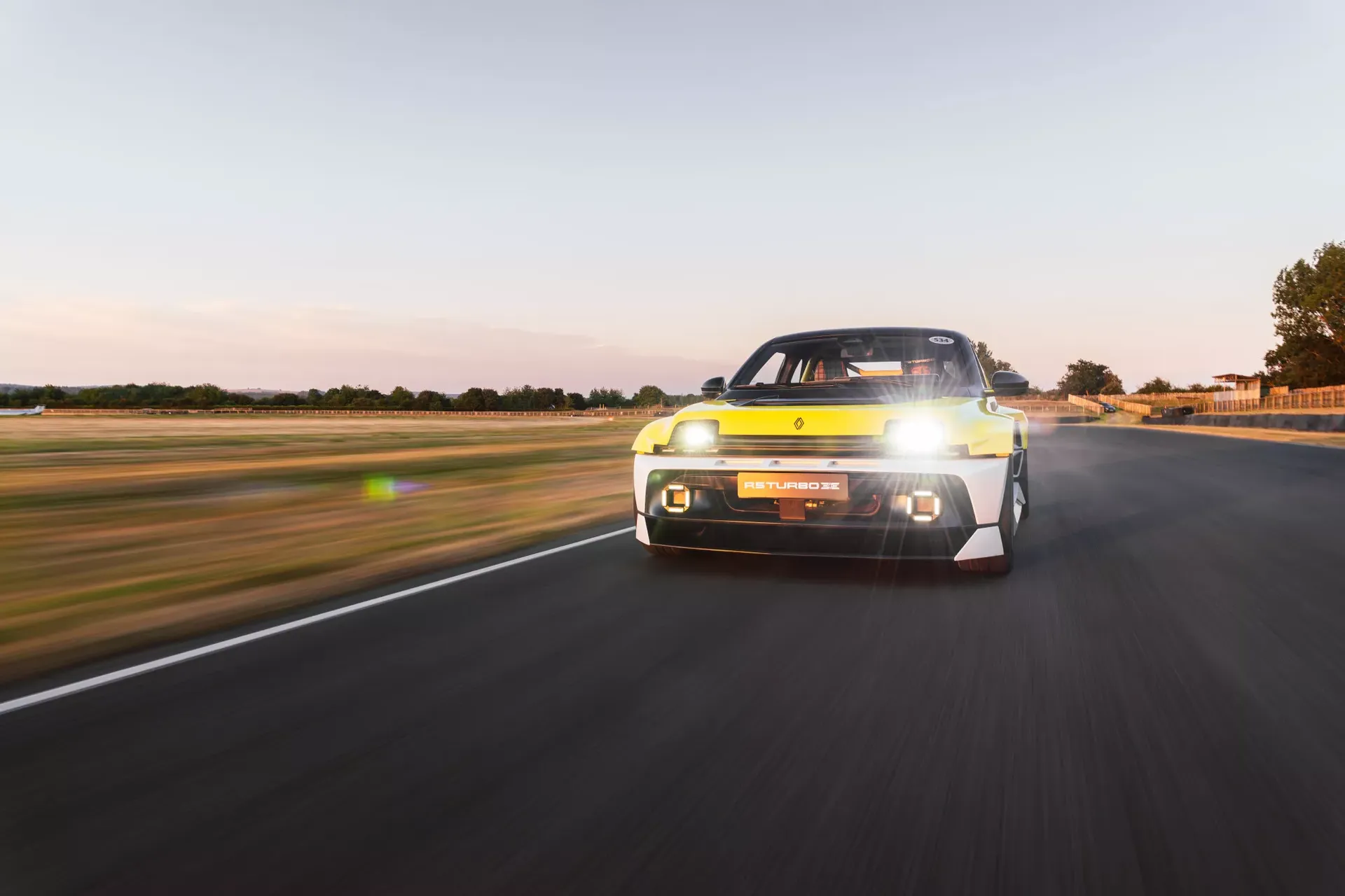 Renault 5 Turbo 3E — żółty egzemplarz, przód, zbliżenie z zapalonymi światłami o zachodzie słońca