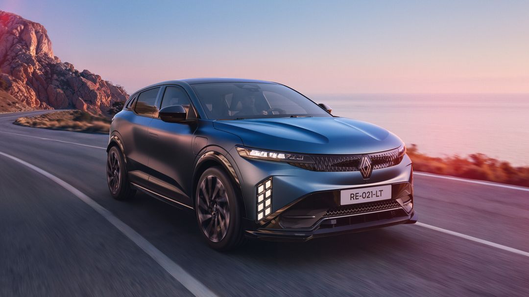 Renault Megane E-Tech Electric — przód, dynamiczna jazda drogą nadmorską o zachodzie słońca