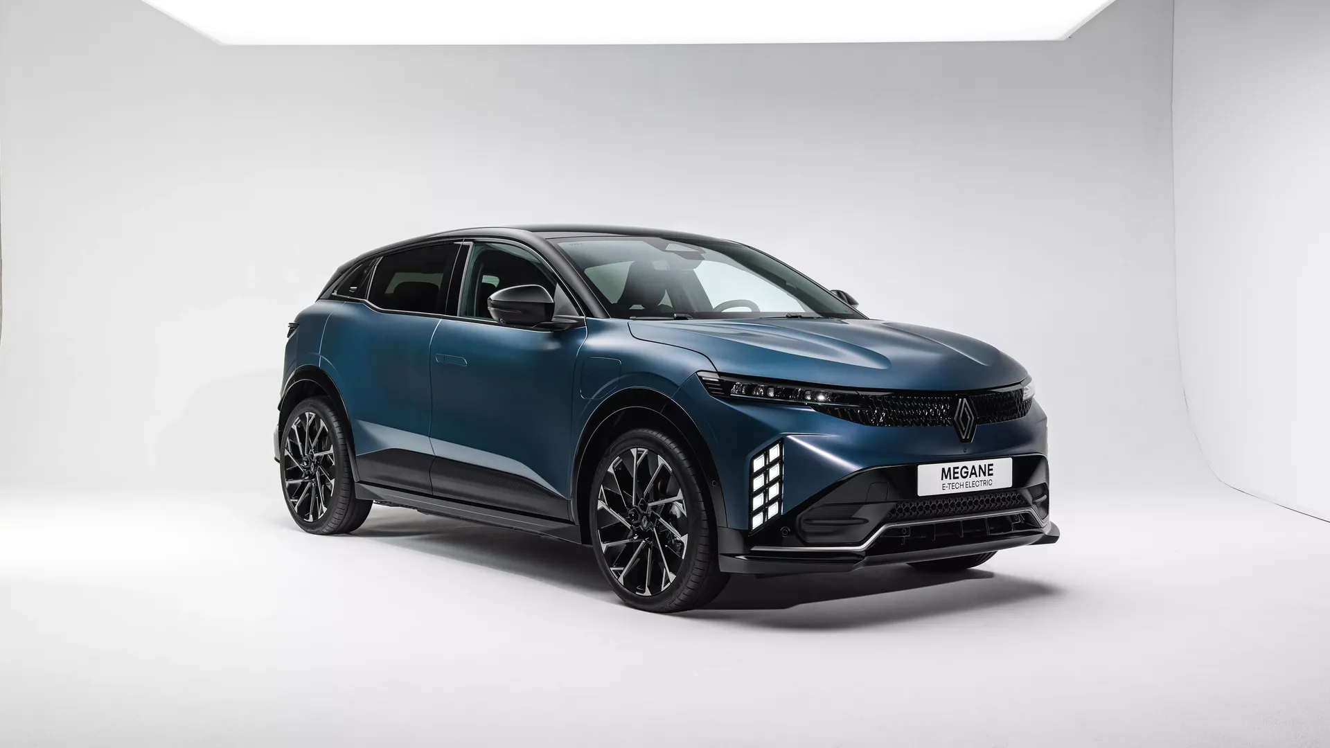 Renault Megane E-Tech Electric — przód/bok, studyjne zdjęcie na jasnym tle z widoczną plakietką modelu