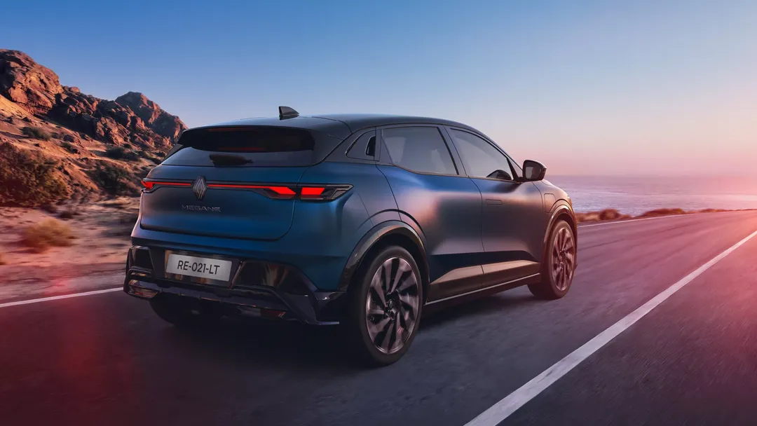 Renault Megane E-Tech Electric — tył/bok, dynamiczna jazda drogą nadmorską o zachodzie słońca