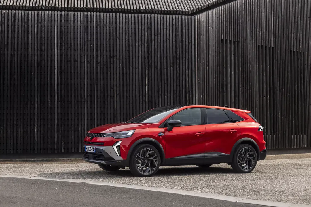 Renault Symbioz — widok z boku, czerwony SUV na tle drewnianej elewacji z listew