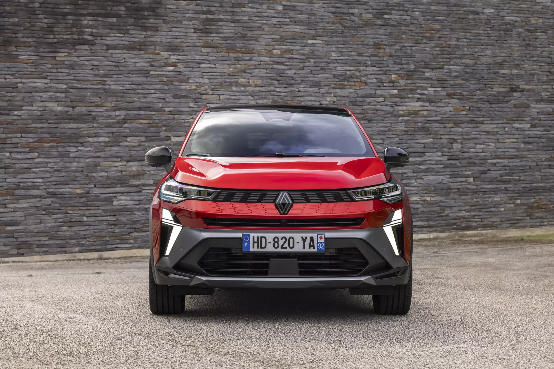 Renault Symbioz — widok przodu na wprost, czerwony SUV na tle kamiennego muru