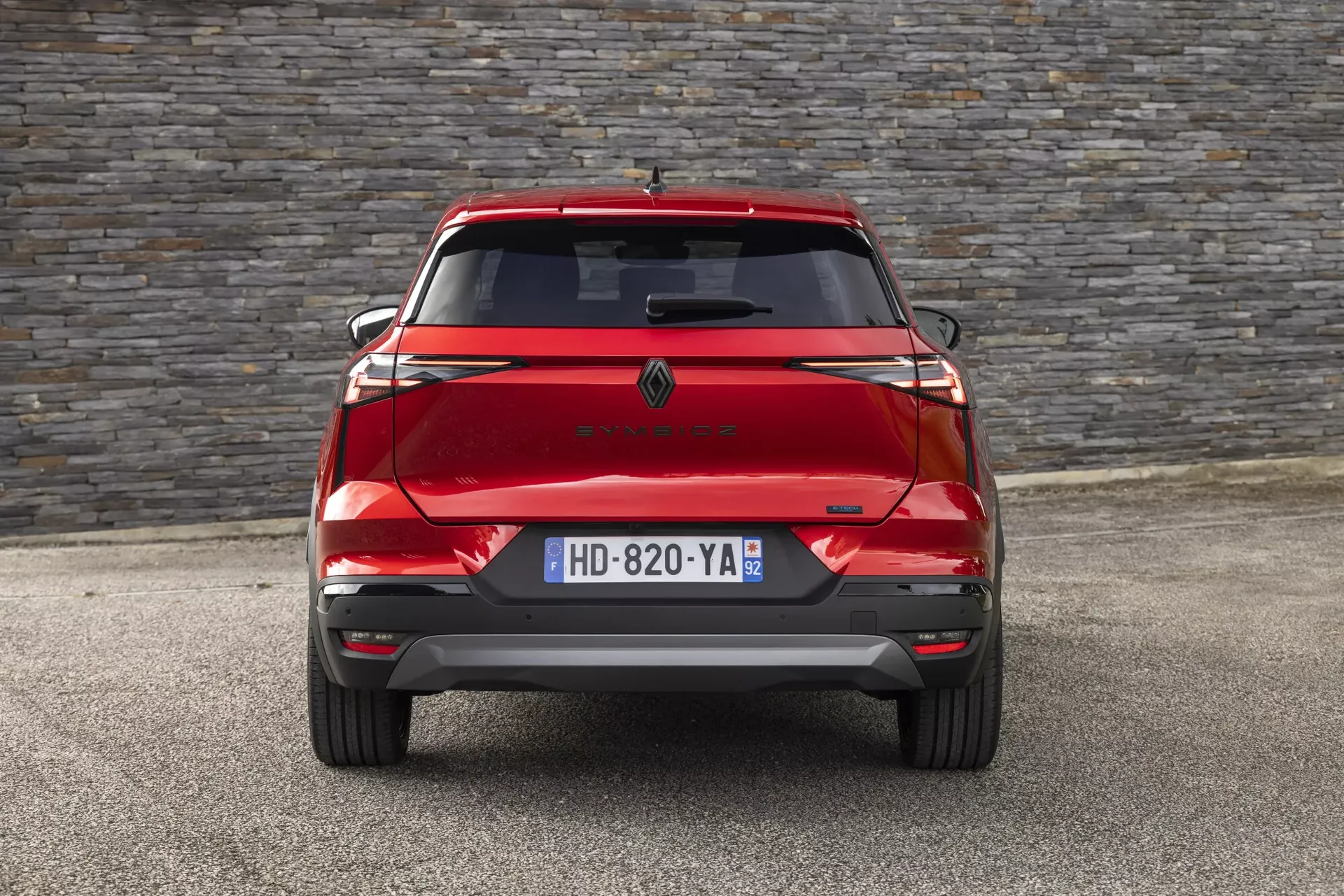 Renault Symbioz — widok tyłu na wprost, czerwony SUV na tle kamiennego muru