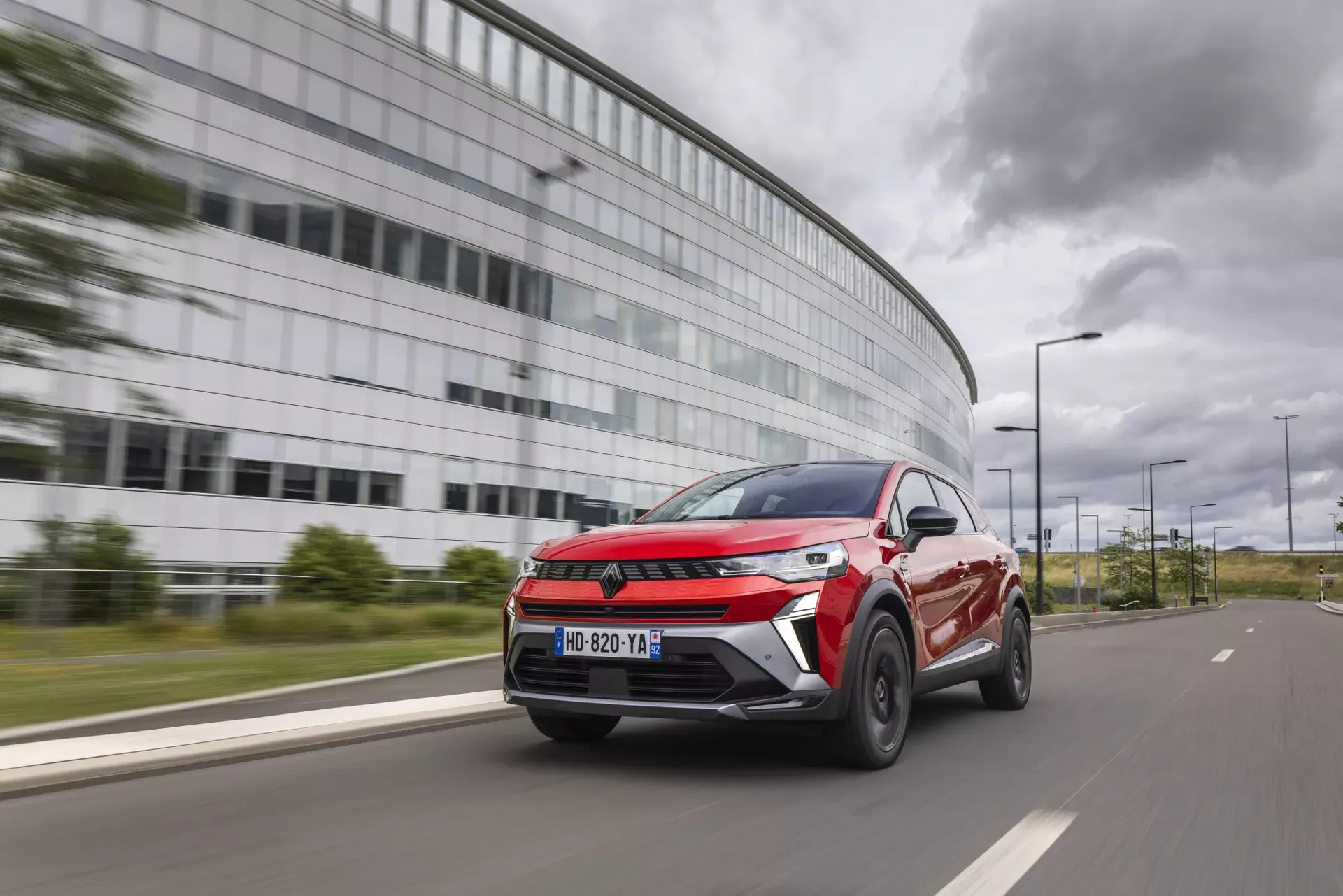 Renault Symbioz — dynamiczna jazda, czerwony SUV na tle nowoczesnego budynku biurowego