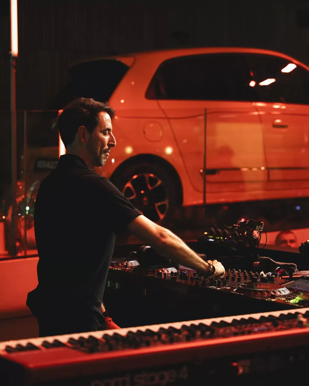 Renault Twingo — bok i tył pojazdu w czerwonym, klimatycznym oświetleniu, w tle DJ przy konsolecie