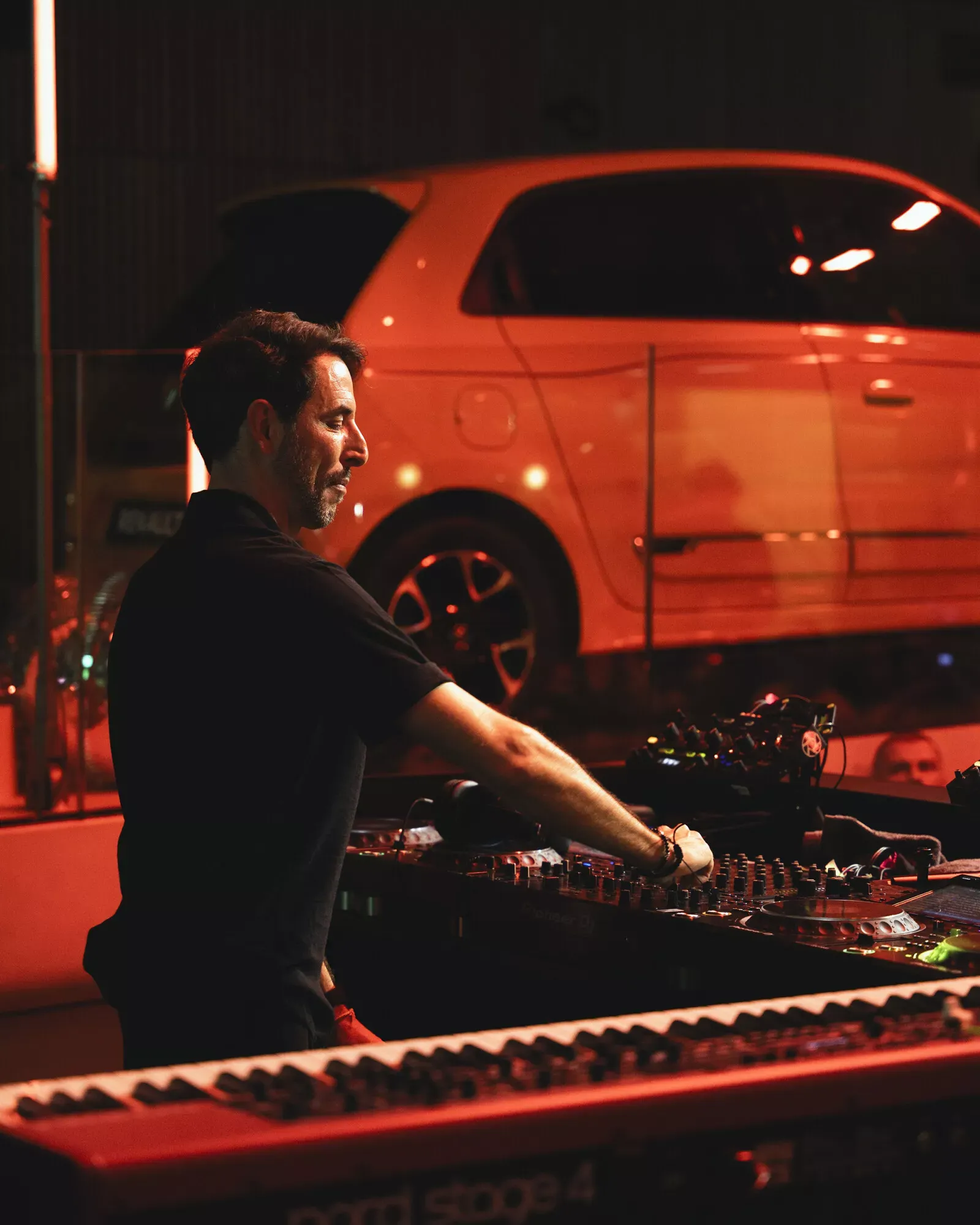 Renault Twingo — bok i tył pojazdu w czerwonym, klimatycznym oświetleniu, w tle DJ przy konsolecie