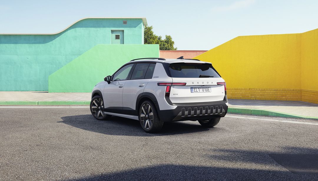 Škoda Epiq — tył 3/4, biały kolor, tablice DE, tło kolorowe ściany