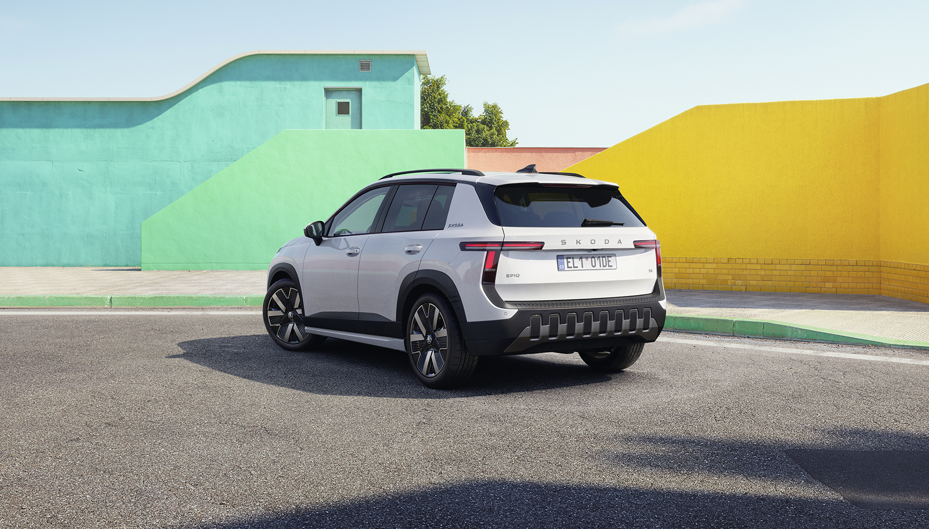 Škoda Epiq — tył 3/4, biały kolor, tablice DE, tło kolorowe ściany
