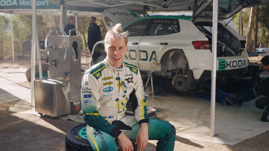 Kierowca rajdowy Škoda Motorsport w kombinezonie, w tle auto serwisowe Škoda na trasie rajdu