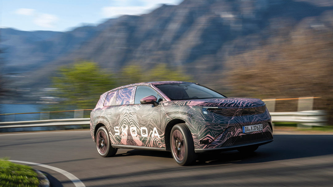 Škoda Peaq — ujęcie 3/4 z przodu lewego, dynamiczna jazda górską drogą, kamuflaż topograficzny, góry w tle