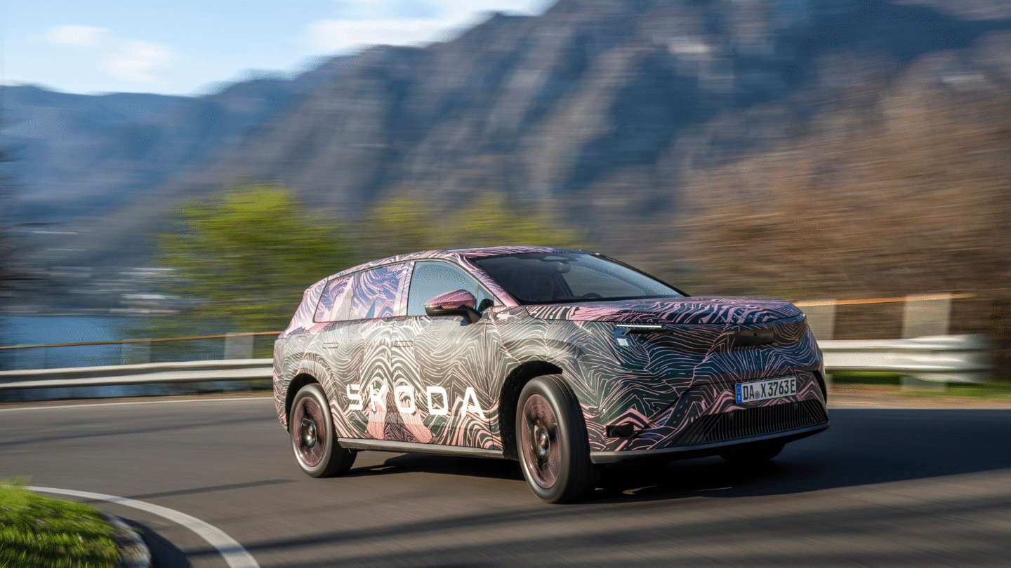 Škoda Peaq — ujęcie 3/4 z przodu lewego, dynamiczna jazda górską drogą, kamuflaż topograficzny, góry w tle