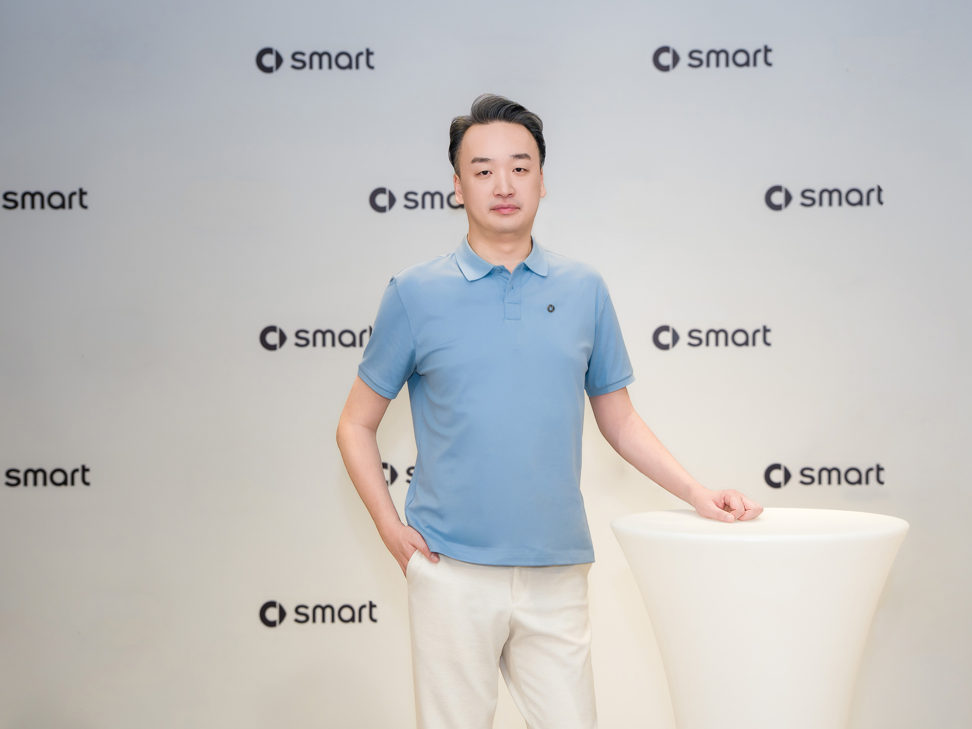 Osoba na tle ściany z powielonym logo smart — ujęcie z eventu, bez samochodu